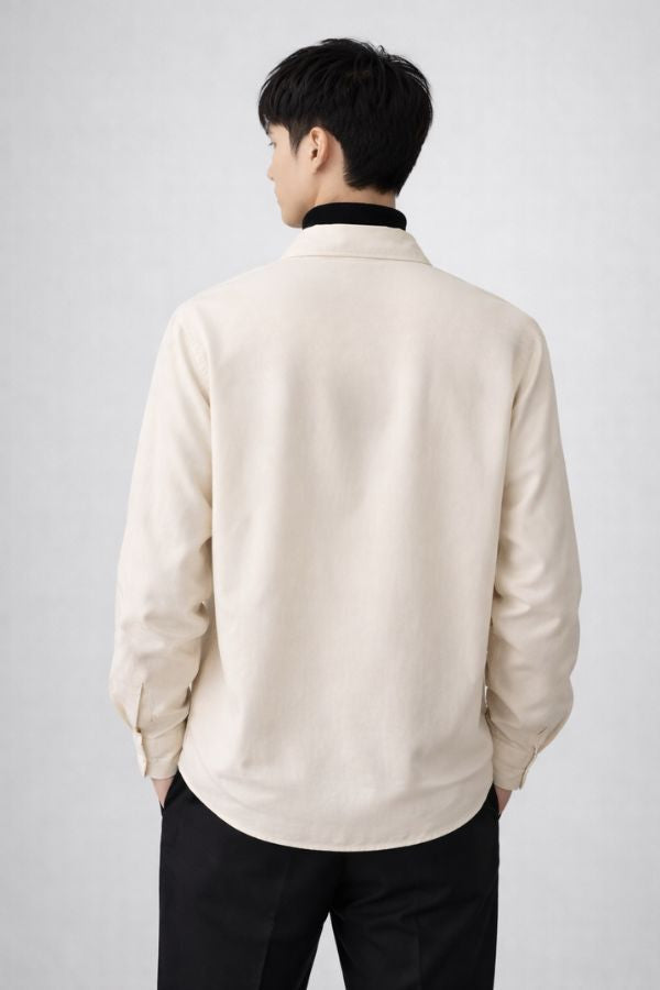 Man wearing a oat colour drop v-neck like shirt over a black turtleneck on a plain background