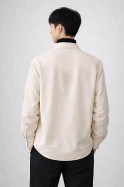 Man wearing a oat colour drop v-neck like shirt over a black turtleneck on a plain background