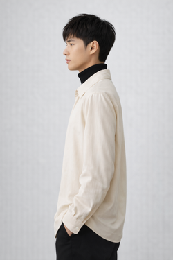 Man wearing a oat colour drop v-nedk like shirt over a black turtleneck on a plain background